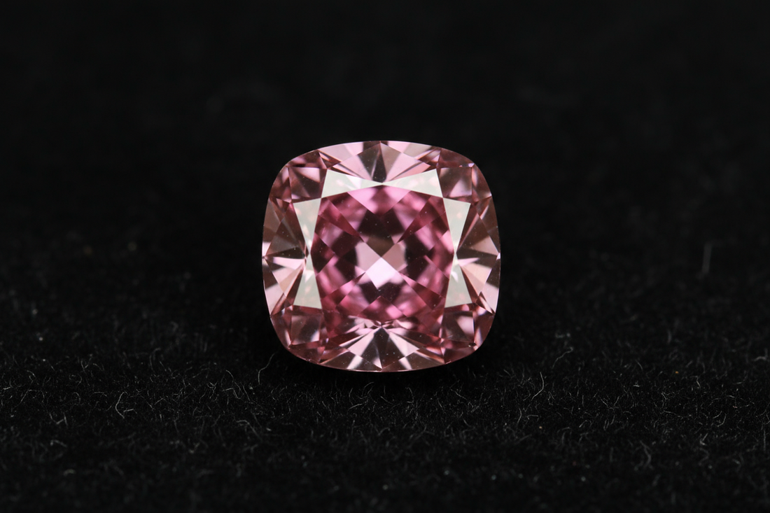 Close-up of a vivid pink diamond on black velvet showcasing its intense color and rarity.