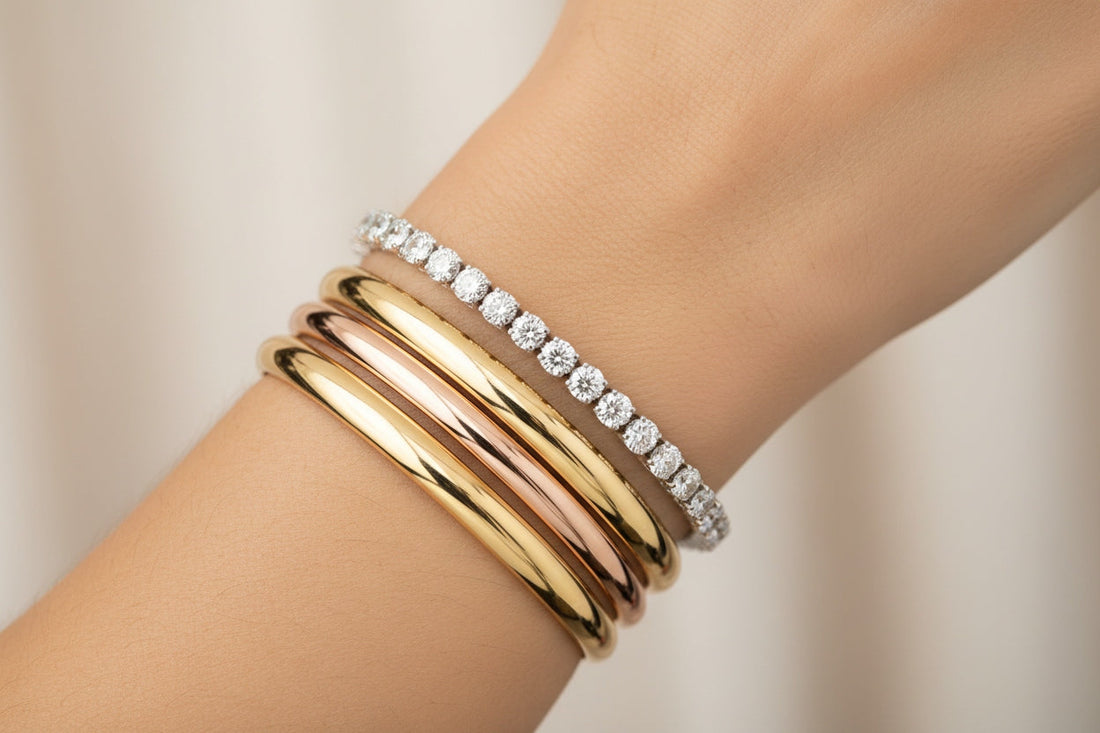 Elegant wrist adorned with a sleek diamond tennis bracelet stacked with polished gold bangles, highlighting the fusion of minimalism and traditional design.