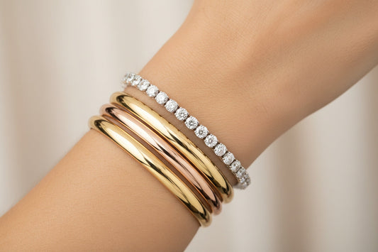 Elegant wrist adorned with a sleek diamond tennis bracelet stacked with polished gold bangles, highlighting the fusion of minimalism and traditional design.